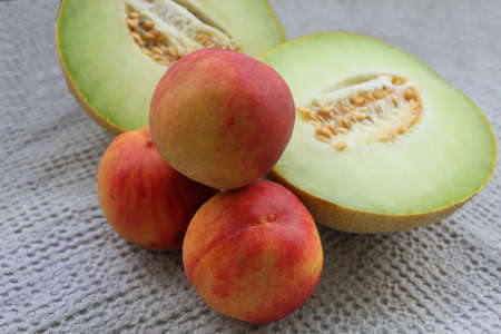 Two halves of melon and peaches on light green tableclothの写真素材