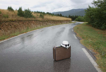 A vintage suitcase and a sun hat on the wet rural roadの写真素材