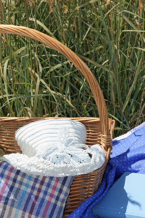 Outdoor picture with a picnic basket, a book and a blue sun hatの写真素材