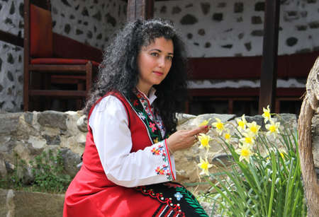 Beautiful young woman dressed in a Bulgarian  traditional folklore costume posing in a garden
