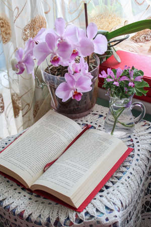 Still life with an orchid pot, a vase with flowers and red books on a clothed tableの写真素材