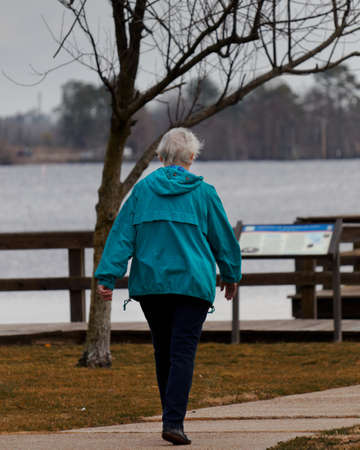 Woman in a blue jacket walking by the waterfront.  Daily walking for exercise.の写真素材