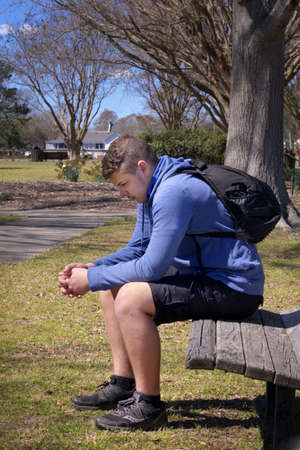 Teenage Boy sitting on a bench outside thinking.  Contemplative. Sad.の写真素材