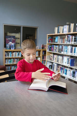 Young Boy Looking at a book in a Libraryの写真素材