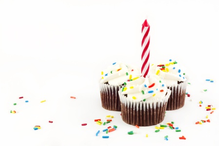 Three chocolate cupcakes with vanilla frosting and sprinkles with one red candle unlit on white background with copy spaceの写真素材
