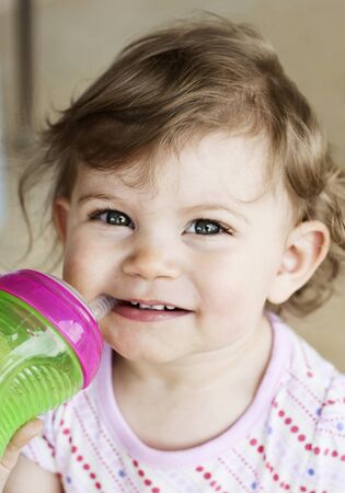 A cute little girl drinking from a sippy cup, selective focus on faceの写真素材