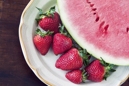 Fresh strawberries and a watermelon slice on a plate, top view on wood tableの写真素材