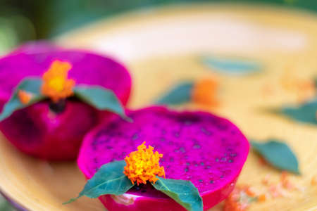 Vibrant colors of Dragon Fruit cut in half displayed on a yellow plate with flowers and leaves for dÃ©cor.の写真素材