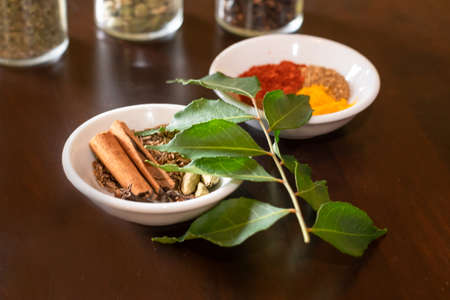Mixture of Asian spices used to make curry displayed on a wooden table with fresh curry leaves as a garish.の写真素材