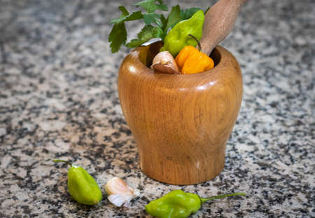 Natural raw organic seasonings. Garlic, green pimento and yellow hot pepper in a mortar and pestle on a granite countertop.の写真素材