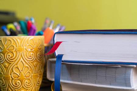Desk with a stack of books with a yellow  mug and pens in the background.の写真素材