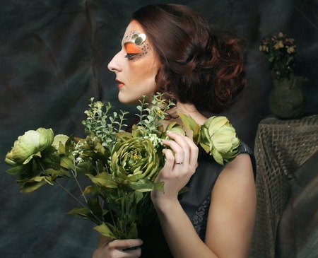 young woman with bright creative make up holding green flowersの写真素材