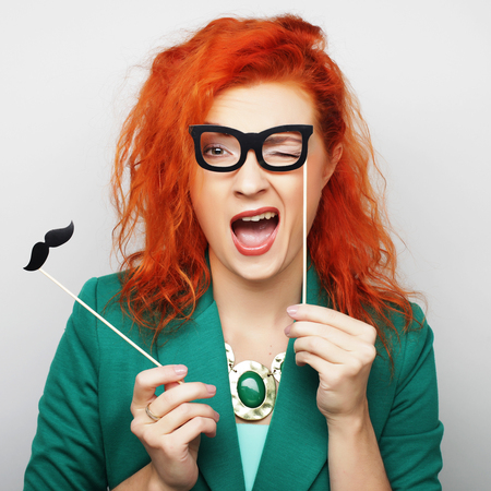 Attractive playful young woman holding mustache and glasses on a stick. Ready for party.の写真素材