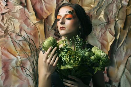 young woman with bright creative make up holding green flowersの写真素材