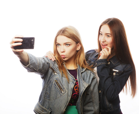 technology, friendship and people concept - two smiling teenagers taking picture with smartphone cameraの写真素材