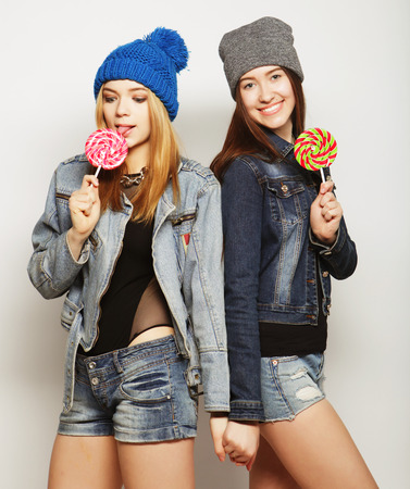 Close up fashion lifestyle portrait of two young hipster girls best friends, holding candys, making funny faces and have good time.の写真素材