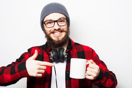 Life style, happiness and people concept: young bearded man with a cup of coffee in hand and showing okey, against grey .の写真素材