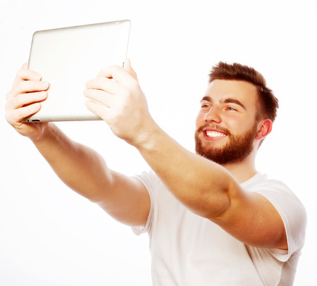 life style, tehnology and people concept: Happy selfie. Young bearded man holding tablet and making photo of himself while standing against white backgroundの写真素材