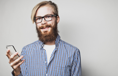life style, happiness and people concept: young bearded man with mobile phone  in hand  against grey background.の写真素材