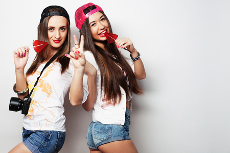 Fashion portrait of two young pretty hipster girls wearing bright make up and holding candys. Studio portrait of two cheerful best friends sisters having fun and making funny faces.の写真素材