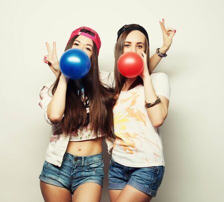 Two happy hipster girls smiling and holding colored balloons over white backgroundの写真素材