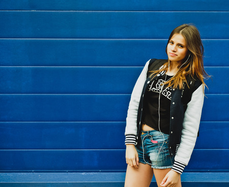 Happy young girl listening music  in headphones over blue wall backgroundの写真素材