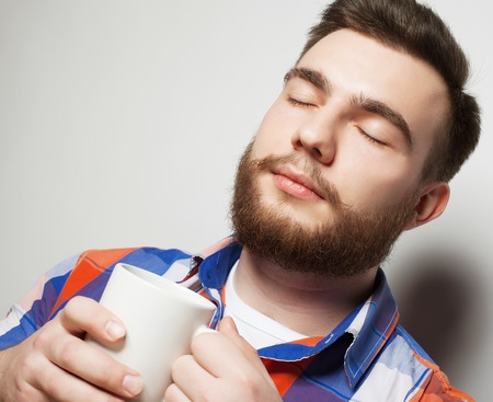 food, happiness and people concept: young bearded man with a cup of coffee against grey backgroundの写真素材