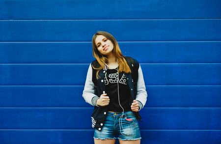 Happy young girl listening music  in headphones over blue wall backgroundの写真素材
