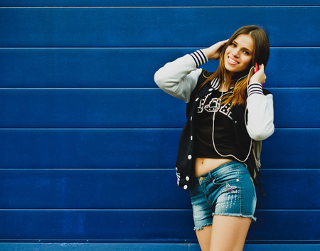 Happy young girl listening music  in headphones over blue wall backgroundの写真素材