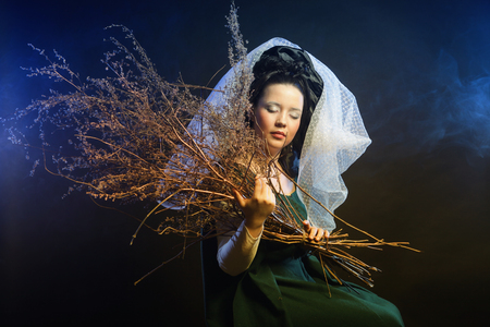 girl in medieval dress  with bunch of sticks in smokeの写真素材