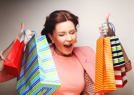 beautiful young woman with colored shopping bags over grey background
