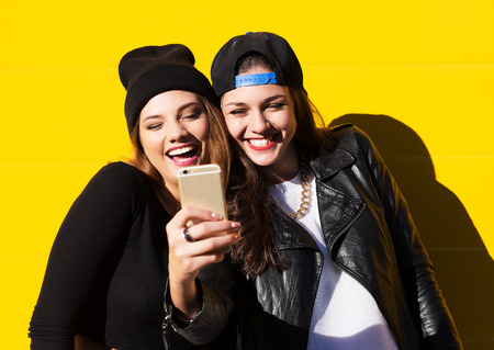 Two teenage girls friends in hipster outfit outdoors make selfie on a phone.