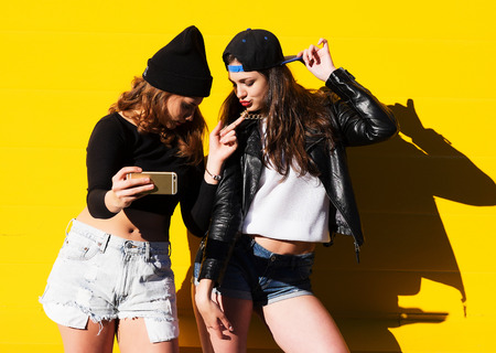 Two teenage girls friends in hipster outfit outdoors make selfie on a phone.の写真素材