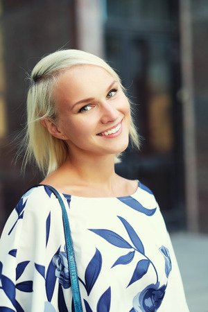 Beautiful blond young woman wearing dress and walking on the streetの写真素材