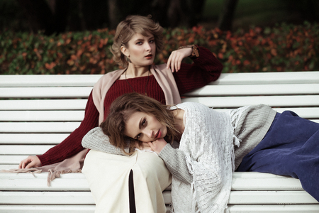 life style, happiness, emotional and people concept: beautiful young women sitting on a bench in the autumn parkの写真素材