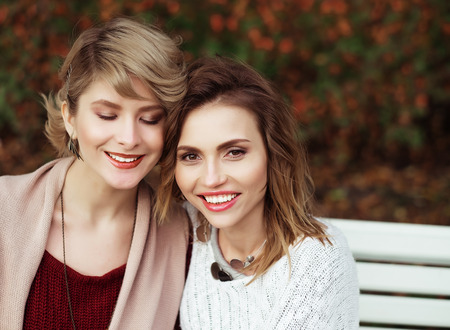 life style, happiness, emotional and people concept: beautiful young women sitting on a bench in the autumn parkの写真素材