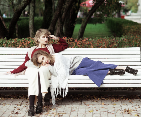 life style, happiness, emotional and people concept: beautiful young women sitting on a bench in the autumn parkの写真素材