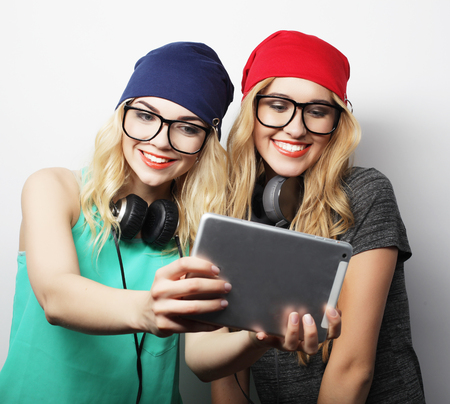 two hipster girls friends taking selfie with digital tablet, studio shot over gray vackgroundの写真素材