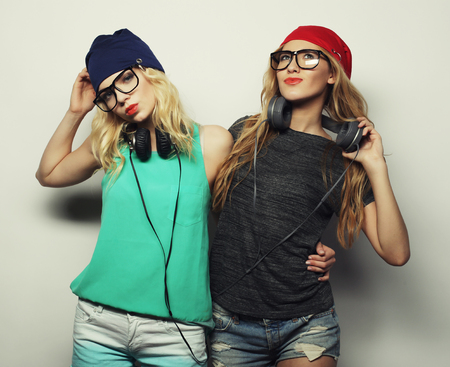 life style, happiness, emotional and people concept: Close up fashion lifestyle portrait of two young hipster girls best friends, wearing bright make up and similar trendy hats, making funny faces.の写真素材