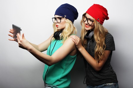 two hipster girls friends taking selfie with digital tablet, studio shot over gray vackgroundの写真素材