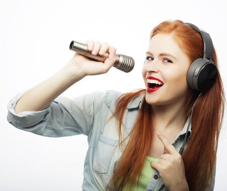 Beautiful young woman with microphone and headphones on gray backgroundの写真素材