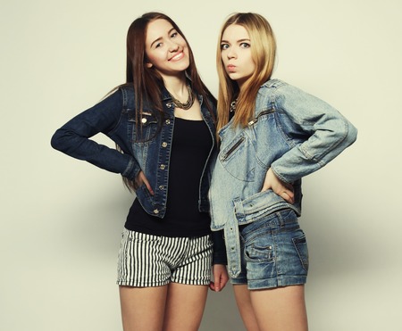 Two young girl hipster friends standing together, having fun.Over grey background.の写真素材