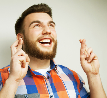 life style and people concept:Waiting for special moment. Portrait of young bearded man in shirt keeping fingers while standing against white background. Hipster style and positive emotions.の写真素材