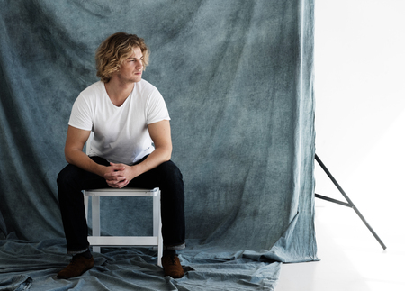 Fashion portrait of young man in white shirt poses in studio over blue backgroundの写真素材