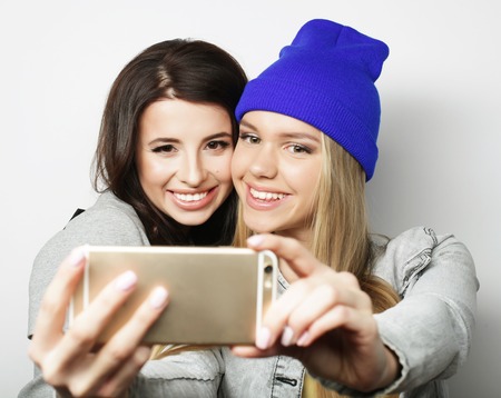 Two teenage girls friends in hipster outfit make selfie over white backgroundの写真素材