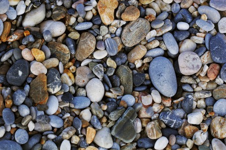 A close up view of smooth polished multicolored stones washed ashore on the beach.
