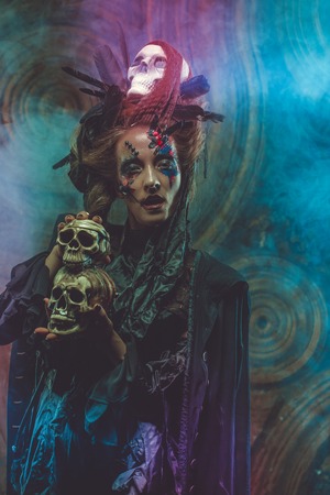 Young  witch hloding skull. Bright make up and  smoke-  halloween theme.の写真素材