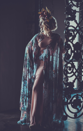 Beautiful woman in a dress of floral colors stands in the palaceの写真素材