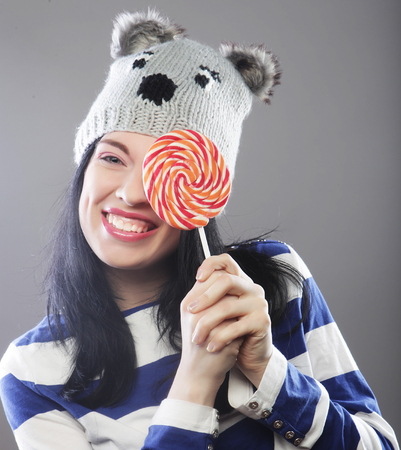 woman wearing hat  looking into the camera and holding a lollipo
