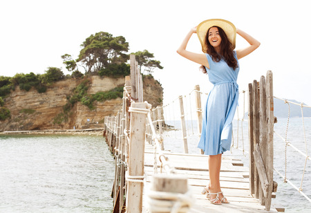 happy woman wearing blue dress and hat on the bridge near seaの写真素材